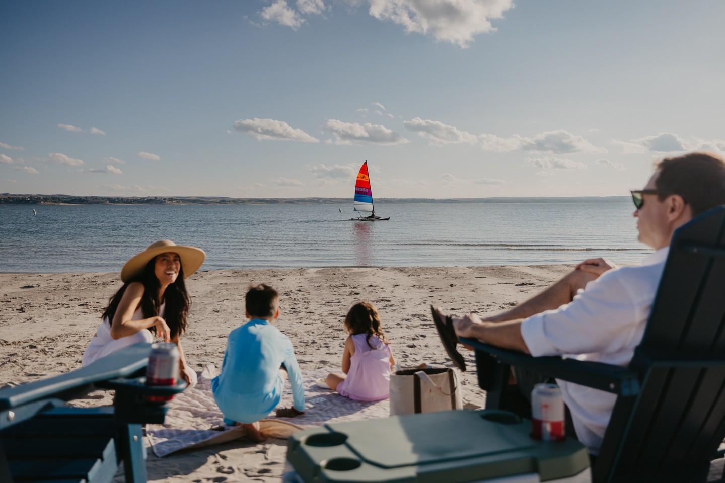 A family enjoying a beach day at Lake McConaughy, with a sailboat in the background on the water.