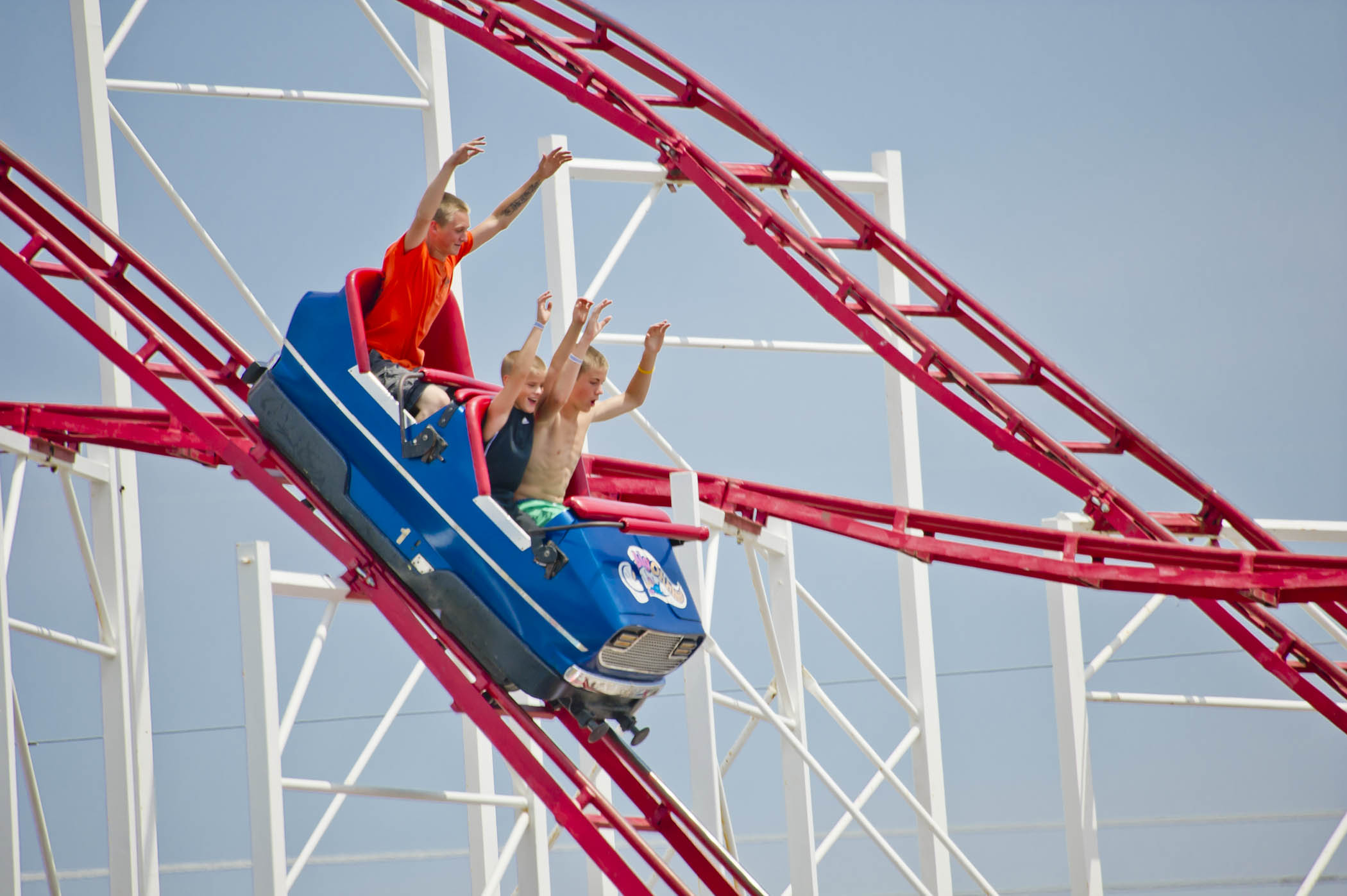 Three kids ride a red and white rollercoaster with their hands in the air at Flex-Plex Waterpark & Rides in Omaha, Nebraska.