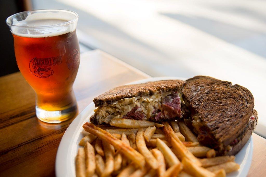 A beer next to a Rueben sandwich and fries from Crescent Moon Ale House.