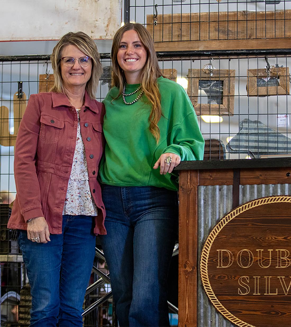 Two women posing next to the Double U Silver boot at Aksarban Stock Show.